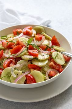 a white bowl filled with cucumbers, tomatoes and onions on top of a table