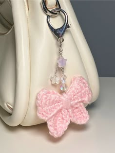 a white purse with a pink crochet bow on it's side and a metal keychain hanging from the front