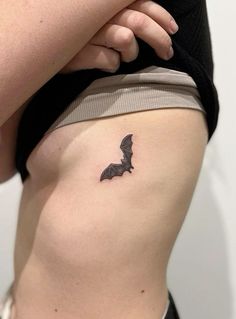 a small bat tattoo on the back of a woman's right side ribcage