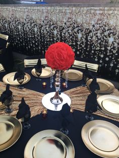 the table is set with black and gold plates, silver place settings, and a red rose centerpiece