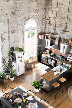 an aerial view of a kitchen and living room with exposed brick walls, hardwood floors, potted plants on the dining table