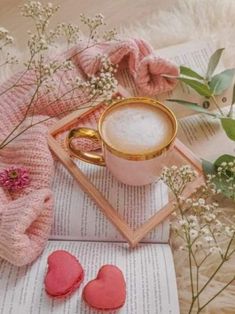 a cup of coffee sitting on top of an open book next to some pink flowers