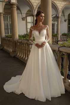 a woman in a white wedding dress standing on a balcony with columns and flowers behind her