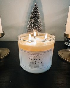 a lit candle sitting on top of a wooden table next to two candles and a small christmas tree