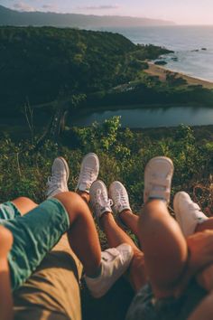 two people sitting on the ground with their feet up in front of them, looking out over water