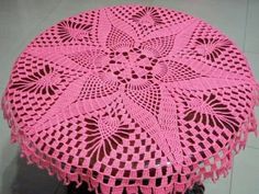 a pink crocheted doily sitting on top of a wooden table next to a white tile floor