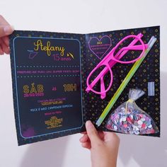 a hand holding an open book with pink glasses on it and candy in the bag