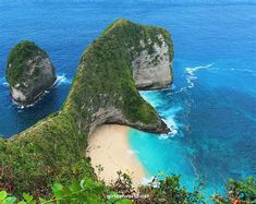 two large rocks sticking out of the ocean next to a sandy beach with blue water