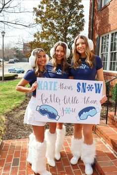 three girls dressed in winter clothes holding a sign