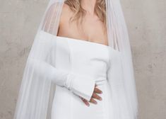 a woman wearing a wedding veil and dress with her hands on her hips, standing in front of a wall