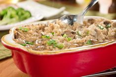 a red casserole dish filled with rice and meat topped with green onion garnish