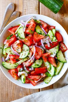 a white bowl filled with cucumber and tomato salad on top of a wooden table