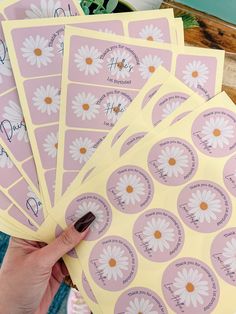 a person holding up six pink stickers with daisies on them