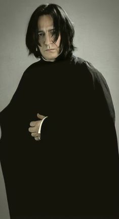 a man in a black cloak with his hands on his chest and one eye open