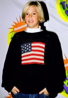 a young boy in an american flag sweater poses for the camera with his hands on his hips