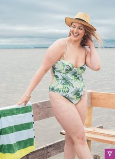 a woman in a green and white one piece swimsuit leaning on a wooden bench