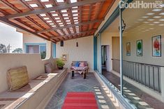 an outdoor covered patio area with red rugs on the floor and wooden slatted roof