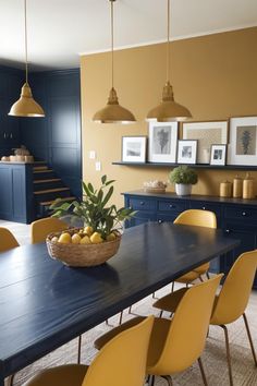 a dining room table with yellow chairs and pictures on the wall above it, along with blue cabinets