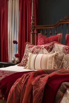 a bed covered in red and white pillows next to a window with curtains on it