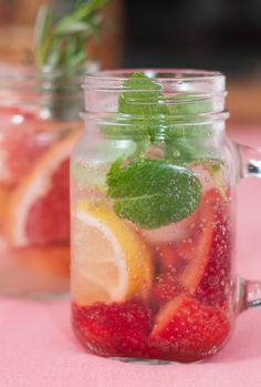 two mason jars filled with fruit and mint garnish on a pink table cloth