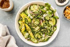 a white bowl filled with cucumbers, onions and other vegetables next to some spices