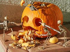 two skeleton figurines in front of a carved pumpkin