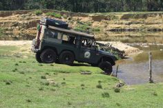 an suv is parked in the grass near a body of water with trees and bushes behind it