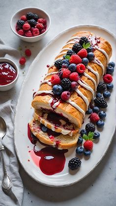 a white plate topped with bread covered in berries and raspberries next to a bowl of fruit