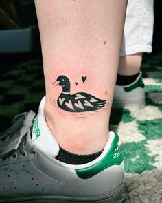 a small duck tattoo on the foot of a person's leg with green and white sneakers