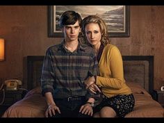 a man and woman sitting on top of a bed next to each other in a bedroom