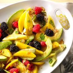 a white plate topped with fruit salad and raspberries on top of a table