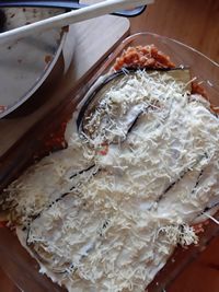 a casserole dish with cheese and meat in it on a wooden table next to a serving utensil