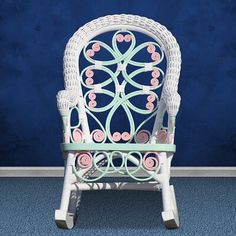 a white wicker chair with pink flowers on it against a blue wall and floor