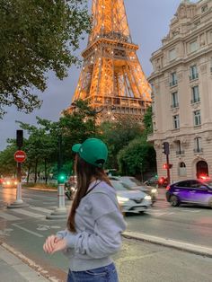 a woman wearing a green hat standing in front of the eiffel tower at night