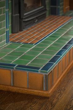 a kitchen counter with green and brown tiles on the top, next to a wood burning stove