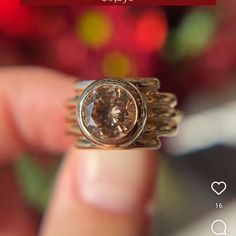 a close up of a person's hand holding a ring with a brown diamond