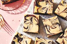 some brownies with white chocolate swirled on them and a pink plate next to it