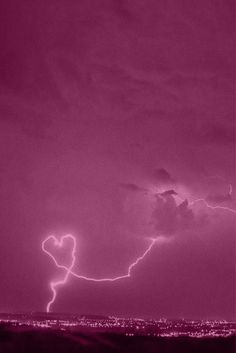 a lightning bolt is seen in the sky over a city at night with pink hues