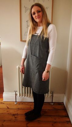 a woman standing in front of a radiator wearing an apron and black tights