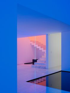 an empty room with blue and pink lighting on the walls, reflecting water in the floor