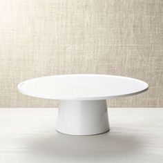 a white cake plate sitting on top of a wooden table next to a beige wall