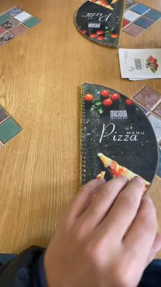 a person holding a piece of pizza in front of a cd on a wooden table