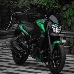 a green and black motorcycle parked on top of a checkered tile floor next to trees