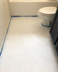 a white bathroom with blue tape on the floor and toilet in the corner, next to a tub