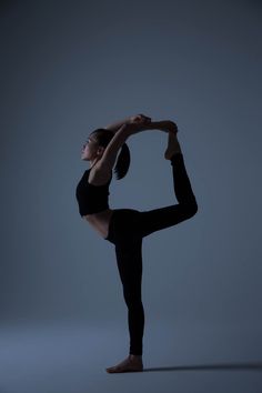 a woman in black is doing a yoga pose with her hands behind her head and legs bent forward