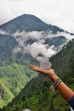 a person holding up a cup in the air with mountains and clouds in the background