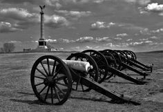 a row of cannon wheels sitting on top of a grass covered field next to a light house