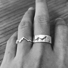 a person's hand wearing a silver ring with mountains on it