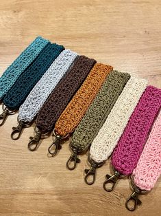 six crocheted key fobs are lined up on a wooden surface