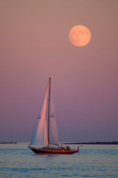 a sailboat with the moon in the background is sailing across the water at dusk